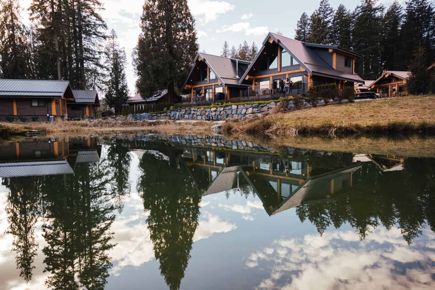 Sandpiper's timber cabins reflected in a still pond, framed by evergreens and muted golden grass